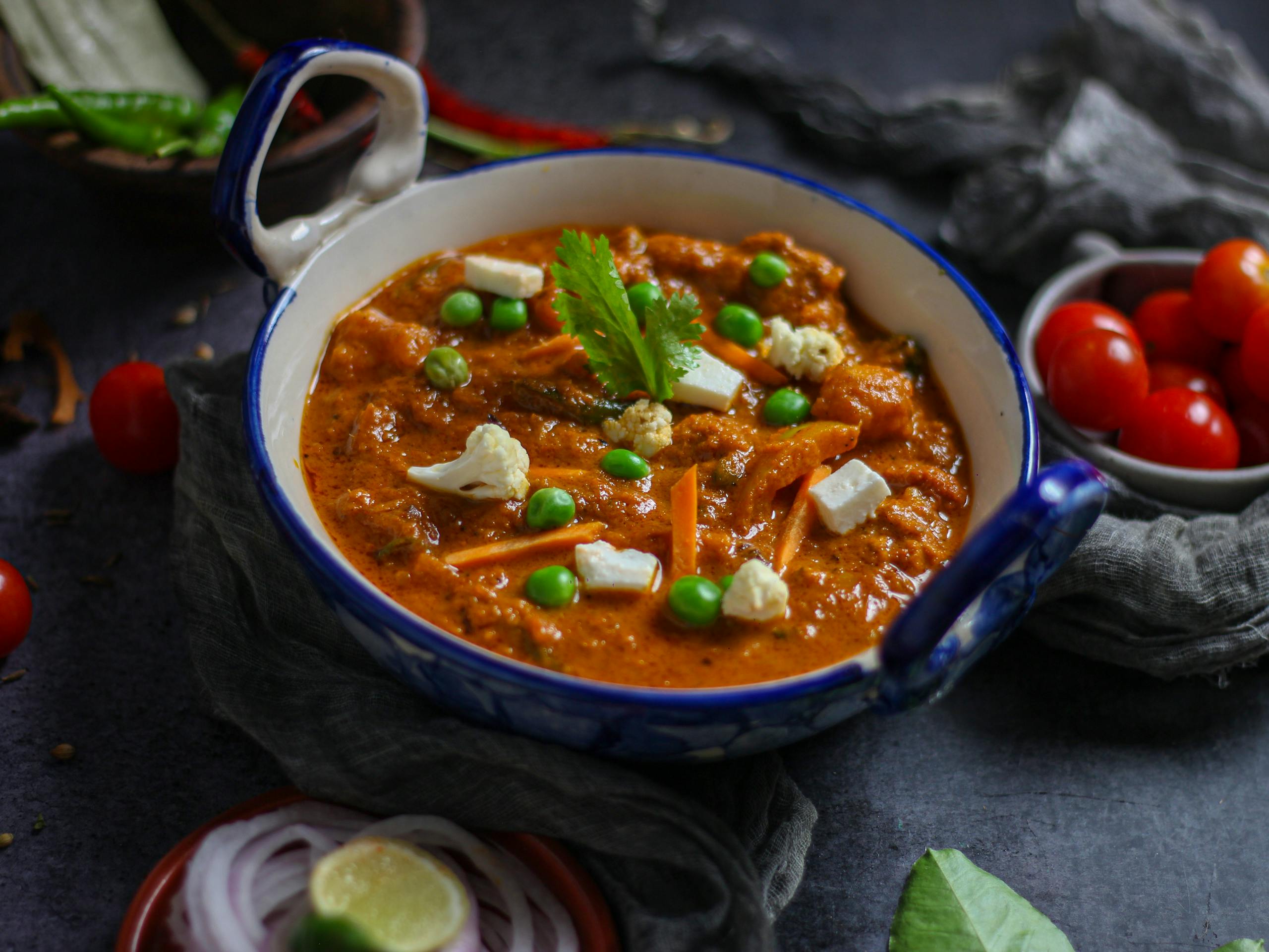 Close-up of vibrant Indian mattar paneer curry with fresh ingredients in a ceramic bowl.